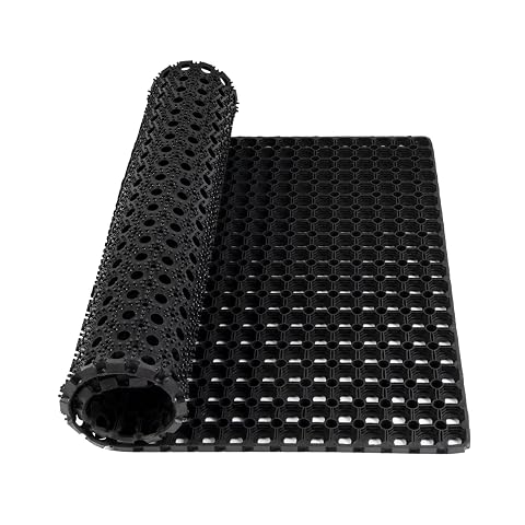 Tapis caillebotis noir en caoutchouc, alvéolé et épais, posé sur une terrasse en pierre humide.