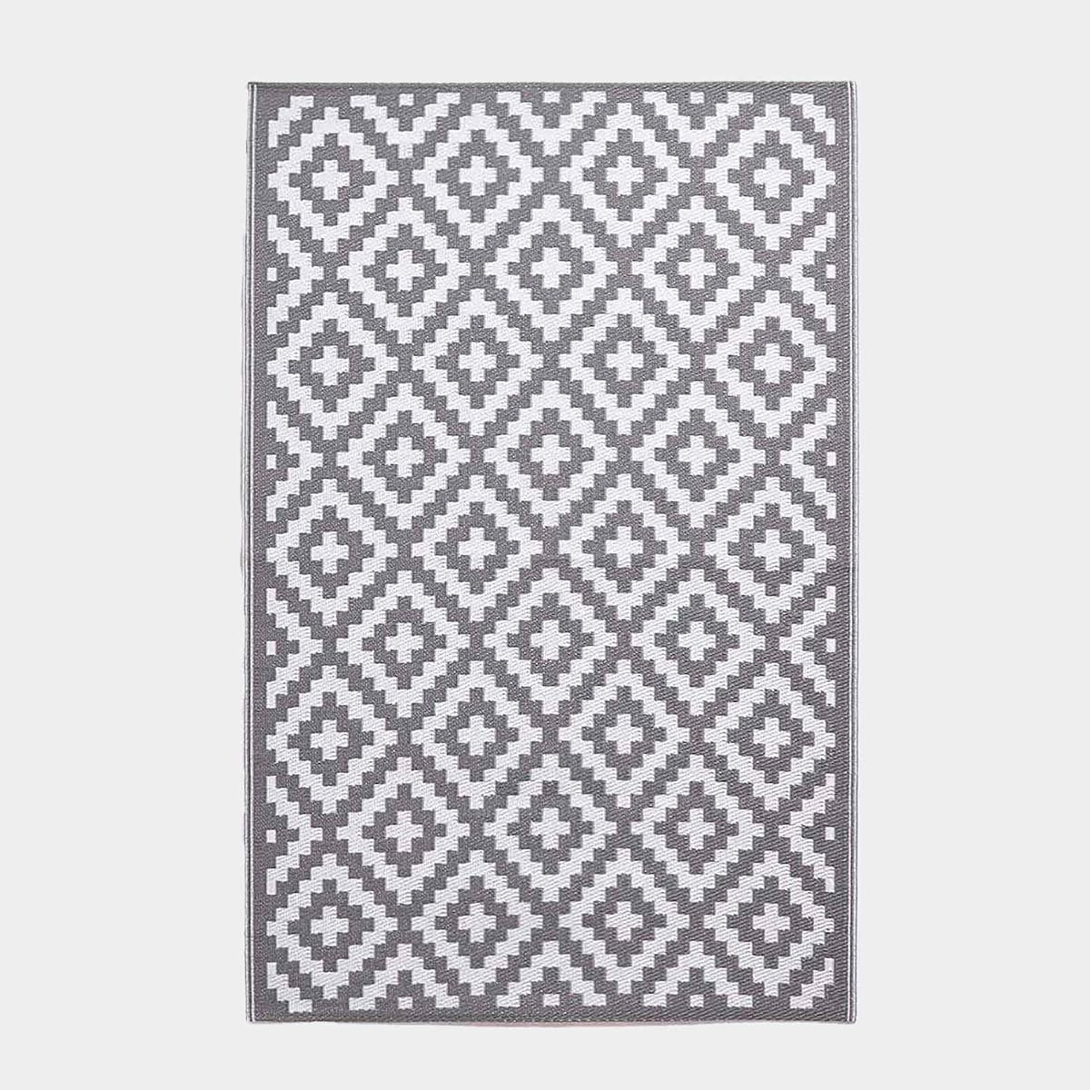 Tapis extérieur réversible gris et blanc à motif géométrique posé sur une terrasse après la pluie