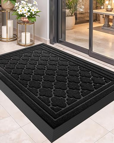 Paillasson rectangulaire noir à motif géométrique posé devant une porte sur une terrasse humide