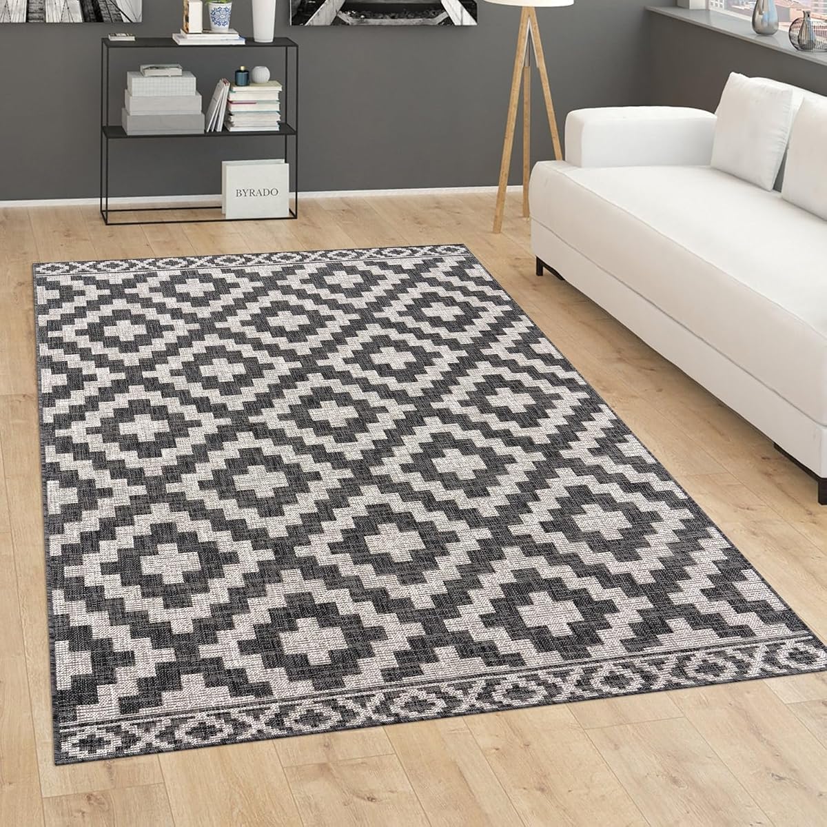 Tapis anthracite à motif géométrique posé sur une terrasse en bois après la pluie.