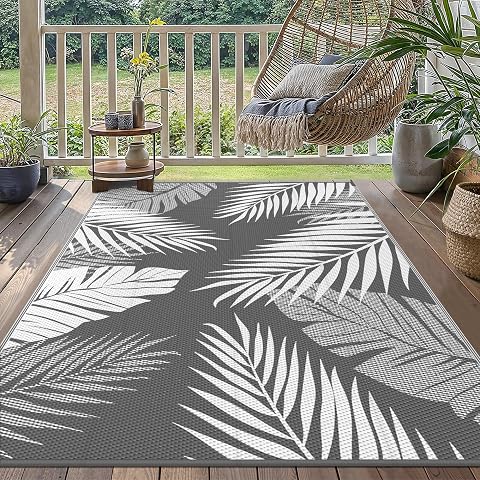 Tapis extérieur réversible à motif de feuilles gris et blanc posé sur une terrasse en bois