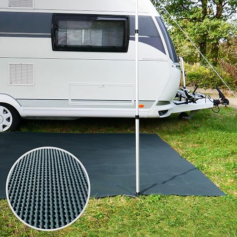 Tapis de camping gris vert ajouré, déployé sous un auvent sur une terrasse en bois après la pluie.